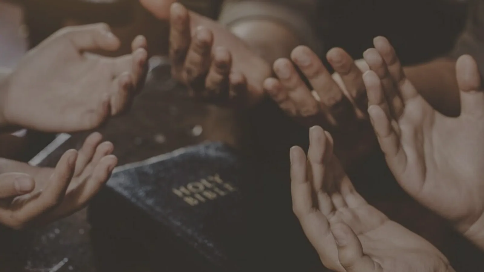 Open hands gathered around a Bible in prayer